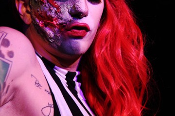 Drag queen performing a halloween show with zombie makeup on half her face and a black and white dress